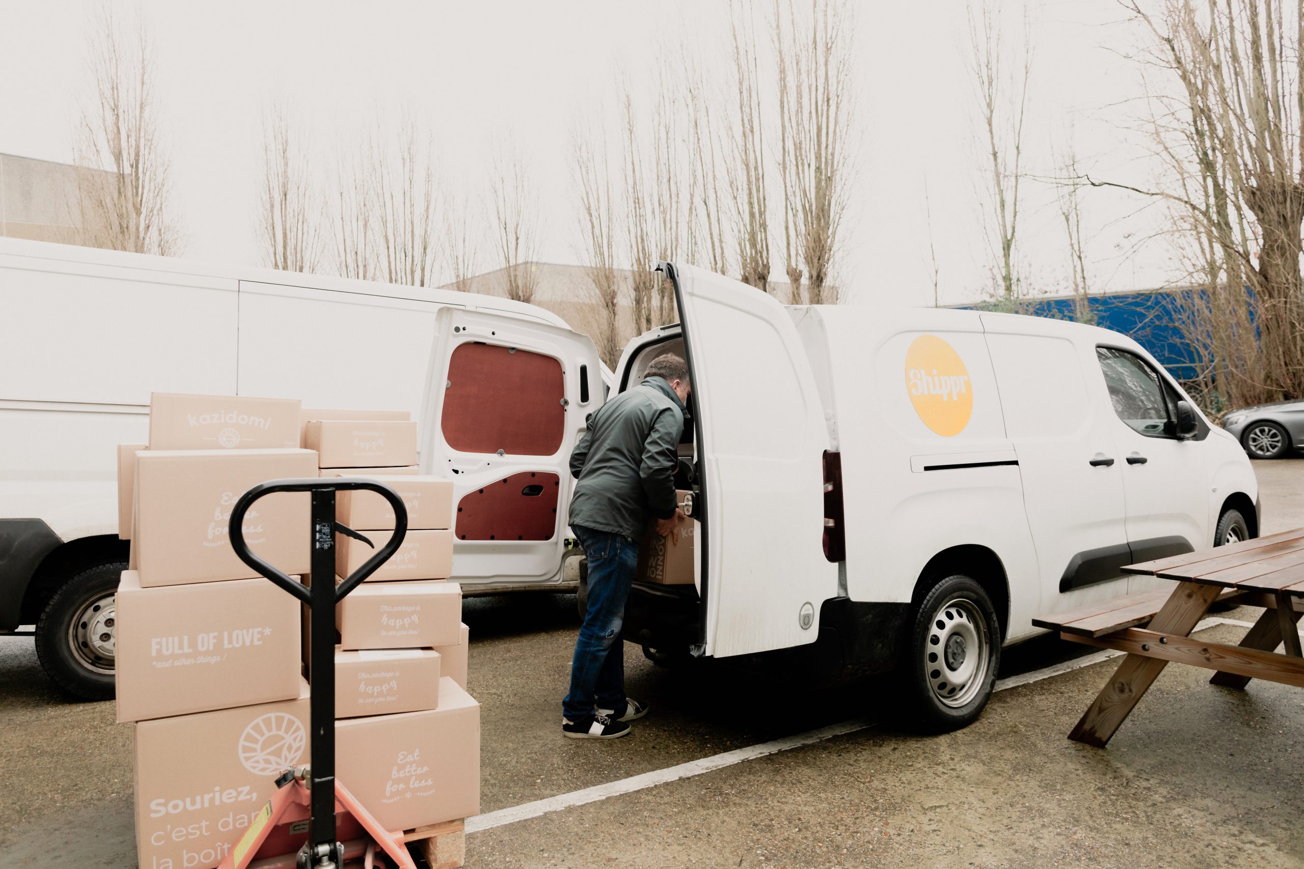 livreur posant des caisses en carton kazidomi dans sa camionnette blanche avec logo shippr
