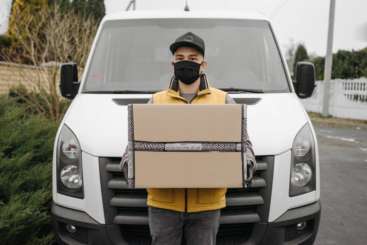 livreur avec capacité de transport de marchandises en masque devant sa camionnette blanche