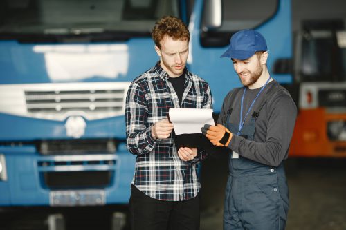 deux chauffeurs livreurs s'échangeant des documents devant un camion frigorifique bleu